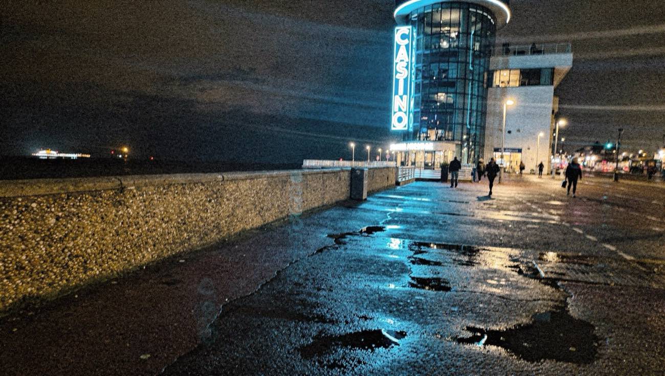 ServerHopCollective exterior with neon reflections on the wet promenade